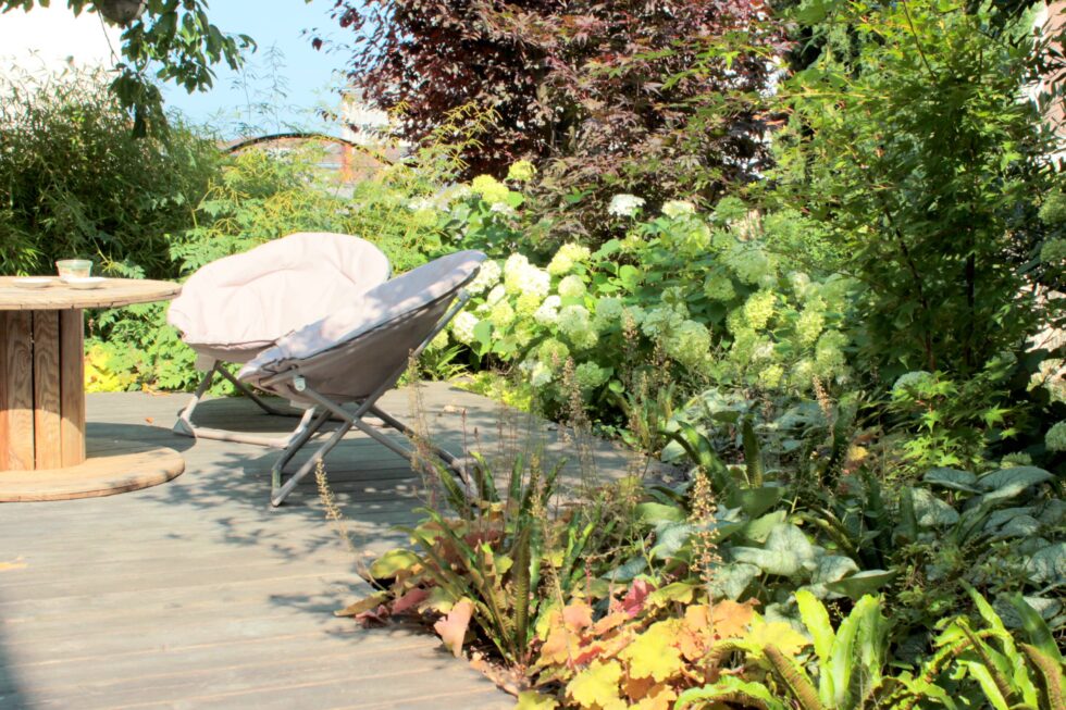 ambiance détente sur une terrasse en bois, dans un écrin de verdure, pour cet aménagement paysager dans un jardin à Mâcon.