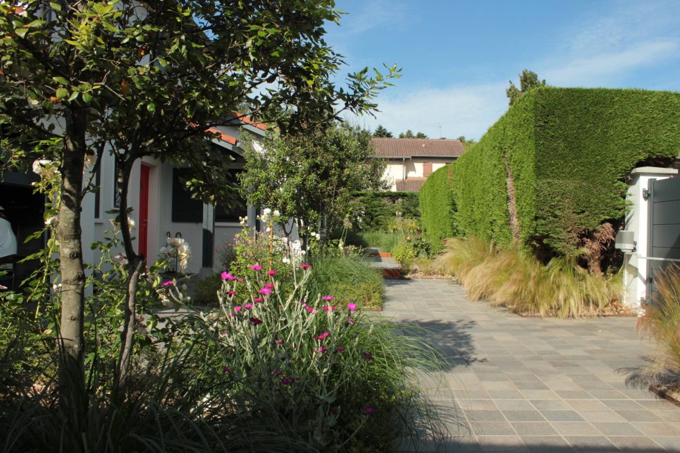 Photo de la cour et accès de cette maison à Saint Didier au Mont d'Or : carreaux petits formats aux teintes nordiques, mis en valeurs par deux grands carrés plantés. Cet aménagement offre une arrivée accueillante et vivante, à pied ou en voiture.