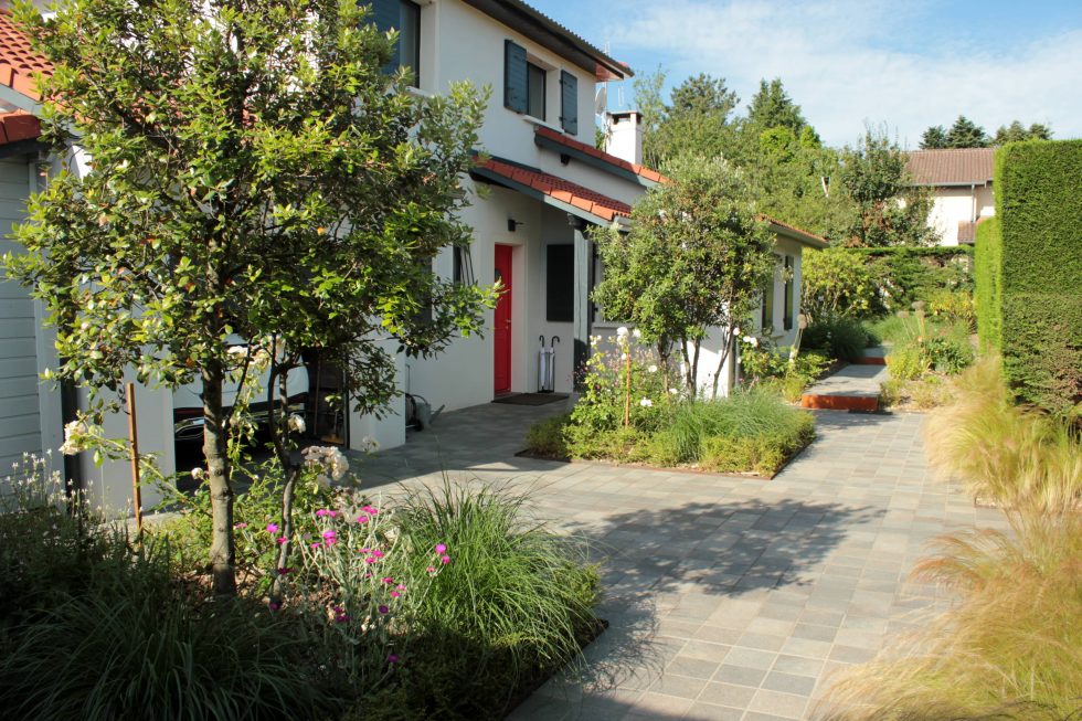 Photo de la cour et accès de cette maison à Saint Didier au Mont d'Or : carreaux petits formats aux teintes nordiques, mis en valeurs par deux grands carrés plantés. Cet aménagement offre une arrivée accueillante et vivante, à pied ou en voiture.