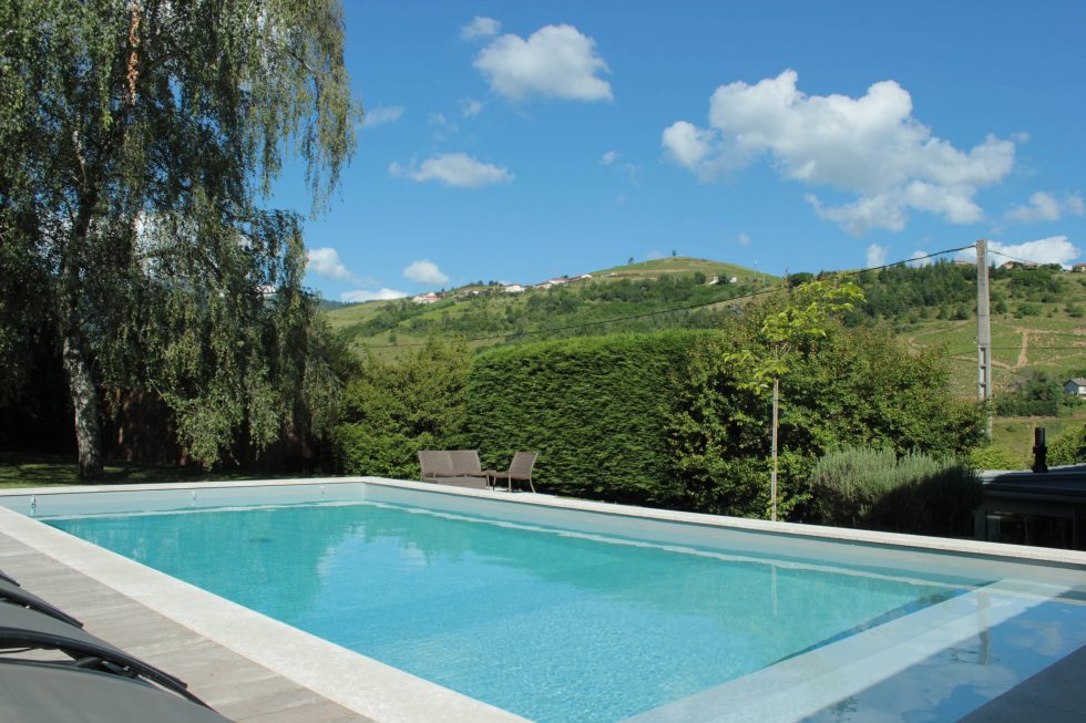 Photo d'une piscine semi-enterrée, avec sa plage réalisée en bois et sa vue sur le paysage, à Vaux en Beaujolais.