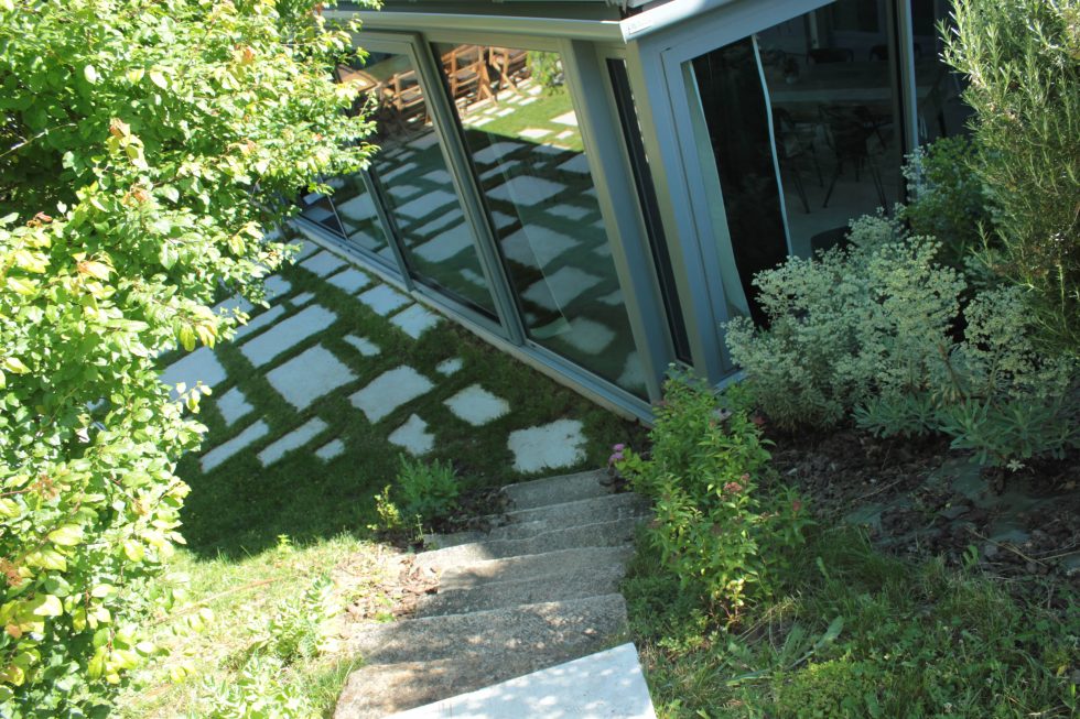 Escalier en pierre donnant sur des dalles de pierre naturelle, dispatchées dans l'herbe.